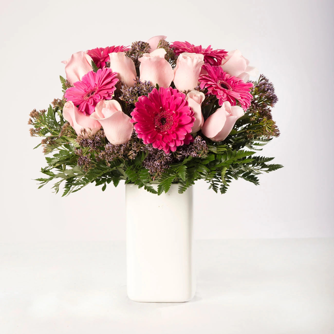 Arreglo de rosas y gerberas rosadas, acompañadas de follaje verde en un florero.