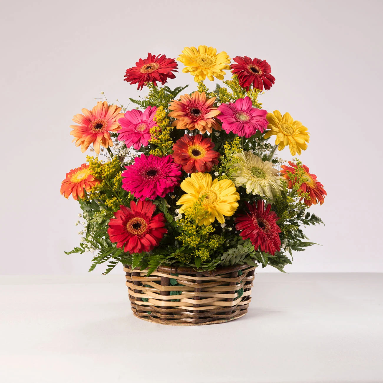 Cesta de mimbre con gerberas de distintos colores acompañadas de follaje verde.