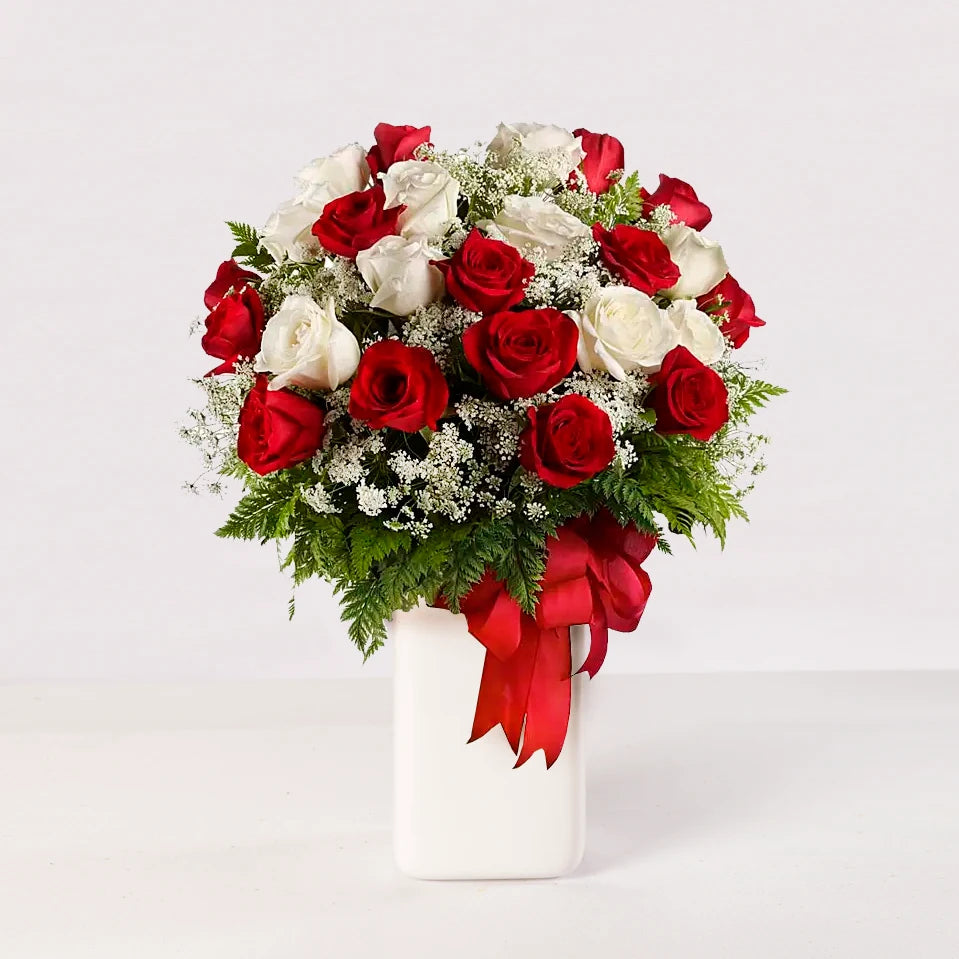 Florero con rosas rojas y blancas, acompañadas de baby breath y follaje verde fino.