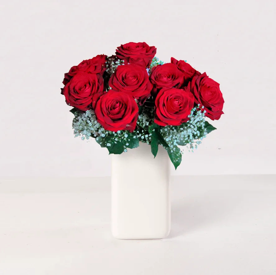 Arreglo de 12 rosas rojas con florero blanco o transparente, con follaje verde variado.