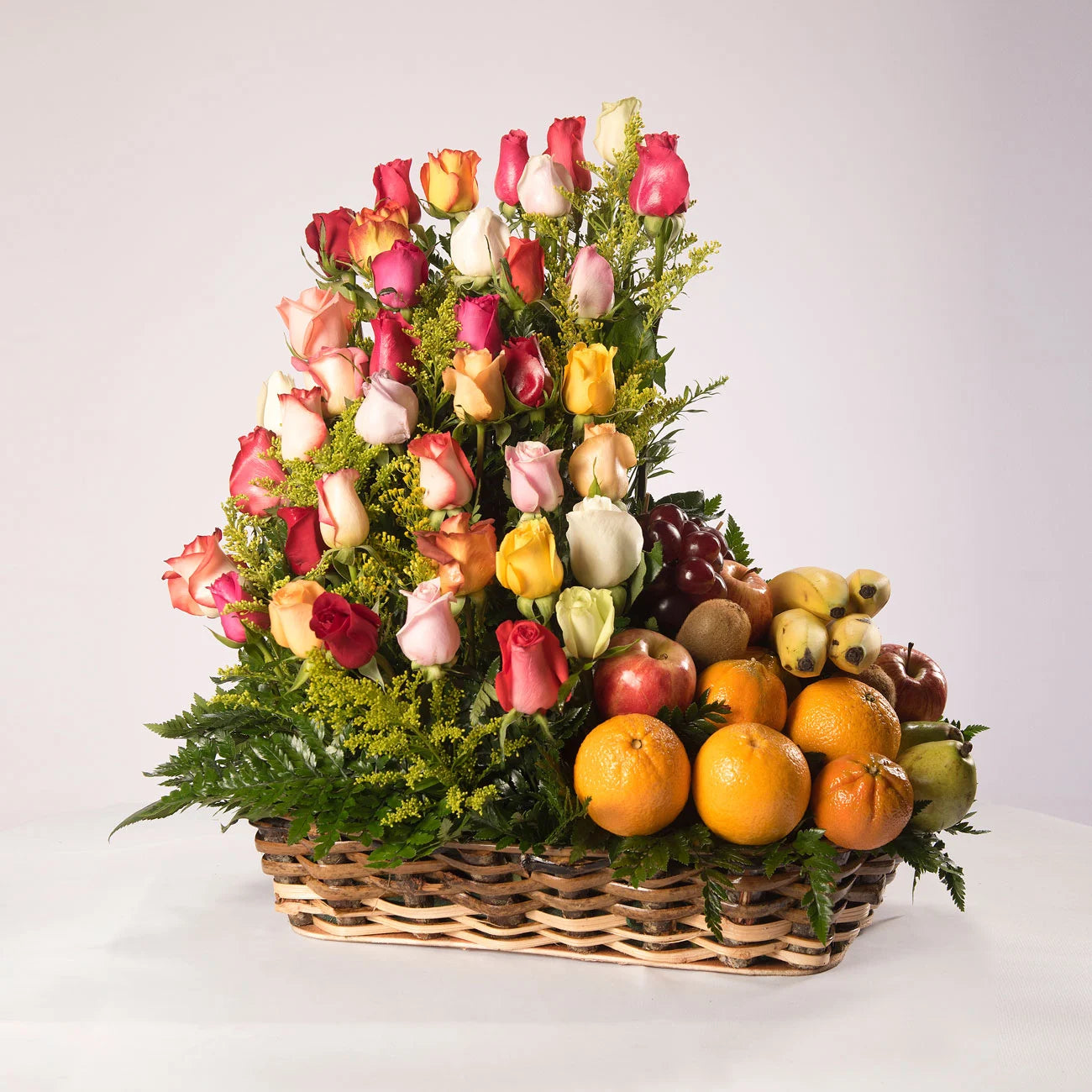 Arreglo de rosas de colores acompañadas con fruta de la temporada sobre una cesta de mimbre.