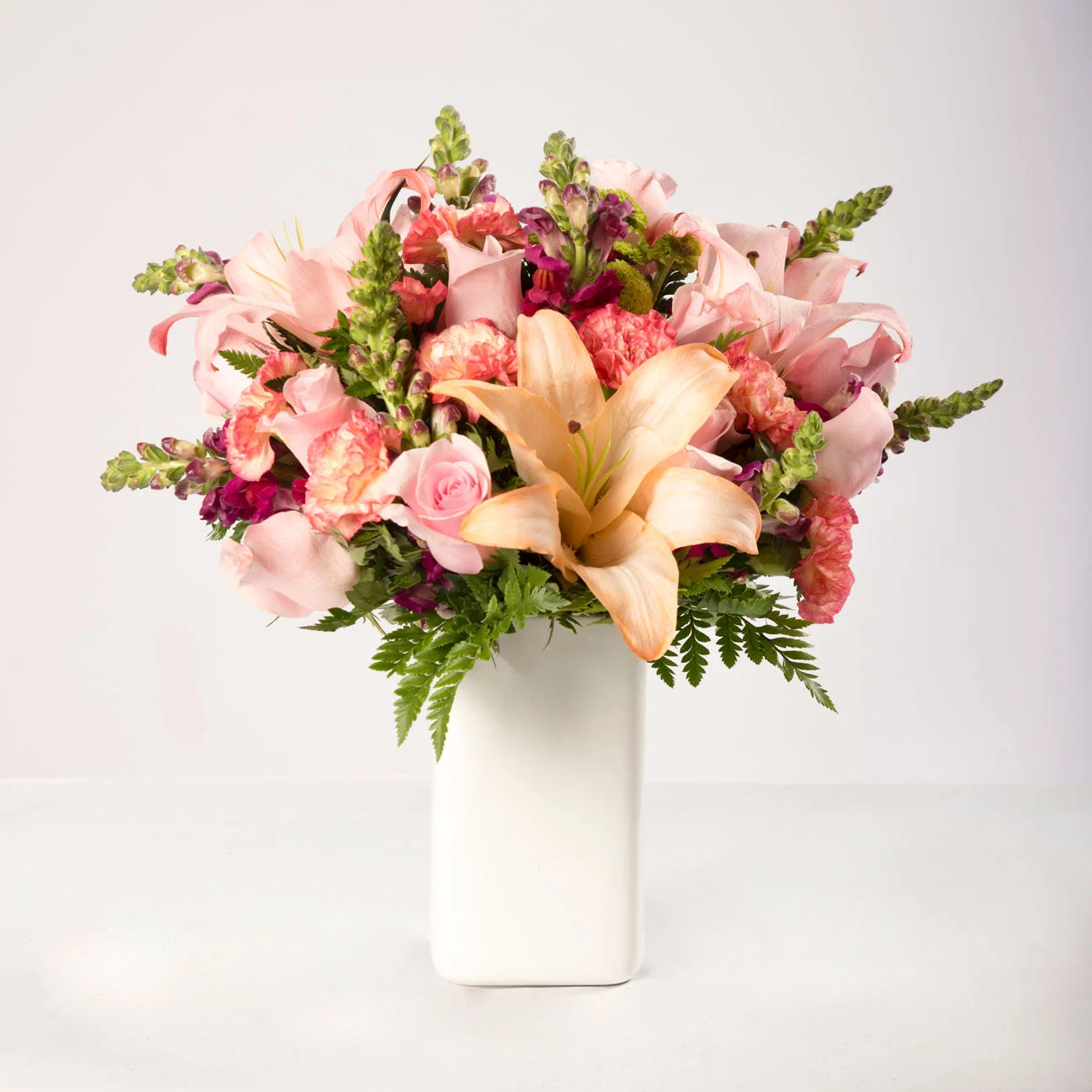 Arreglo de lirios, claveles y rosas rosadas, con follaje verde en un florero