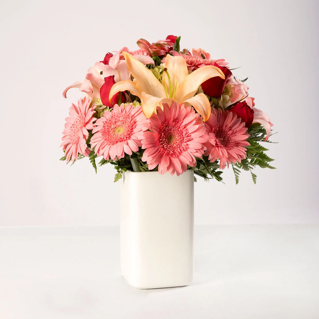 Arreglo de gerberas rosadas, lirios, rosas rojas y claveles en un florero