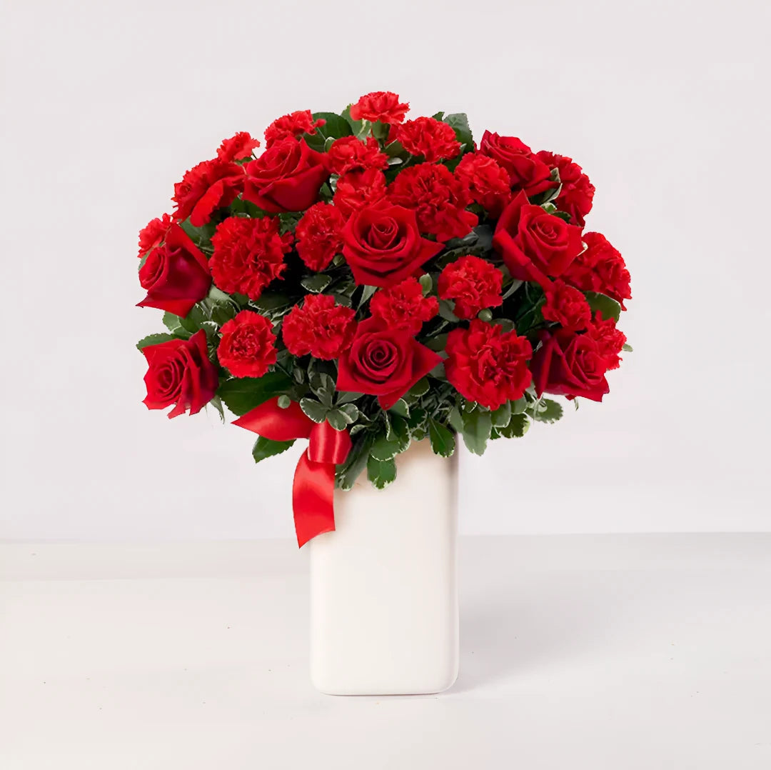 Florero con rosas rojas y claveles rojos.