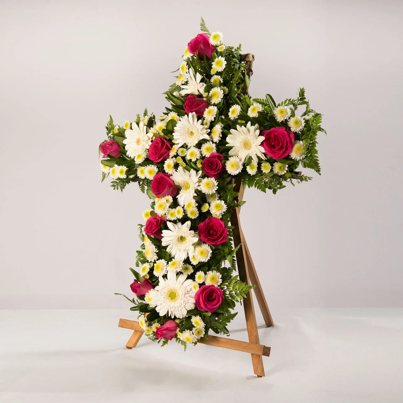 Arreglo fúnebre en forma de cruz con rosas rojas, gerberas blancas y centro verde.