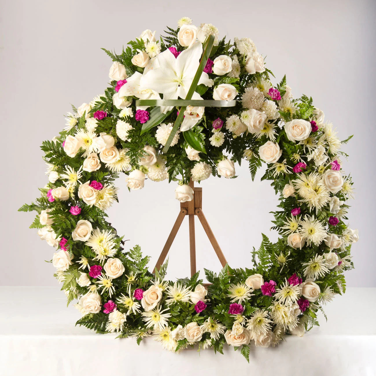 Corona fúnebre acompañada de flores blancas diversas y toques de color rojo o fucsia.