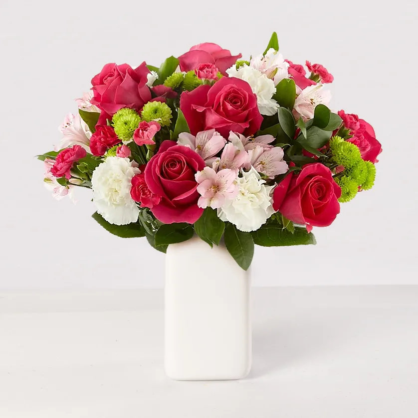Arreglo de rosas y claveles fucsias, claveles blancos, astromelias y centro verde, en un florero.